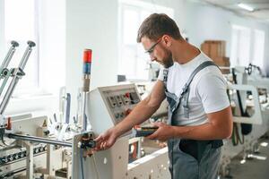 Standing, by the machine. Handsome man is working at the factory of creating eco boxes photo
