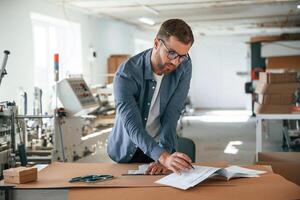 Standing ,by, the table. Handsome man is working at the factory of creating eco boxes photo