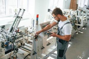 Standing by, the machine. Handsome man is working at the factory of creating eco boxes photo
