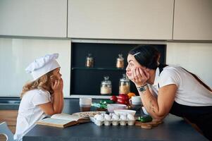 Standing and watching at each other. Mother with her daughter are preparing food on the kitchen photo