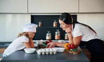 Standing and watching at each other... Mother with her daughter are preparing food on the kitchen,. photo