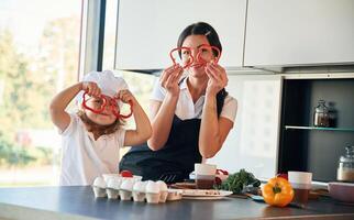 Playing, with ,slices of pepper. Mother, with her daughter are preparing food on the kitchen photo