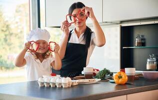 Playing ,with ,slices of pepper. Mother with her daughter are preparing food on the kitchen photo