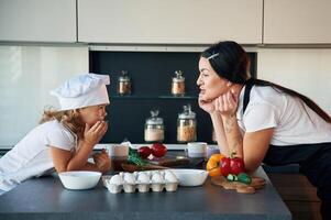 Standing and watching at each other... Mother with her daughter are preparing food on the kitchen, photo