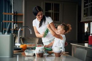 Process of learning.. Mother with her daughter are preparing food on the kitchen photo