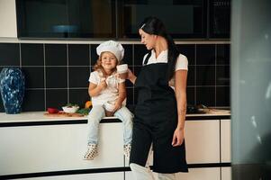 Drinking, from the cups. Mother with her daughter are preparing food on the kitchen photo