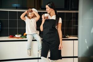 Drinking ,from the cups. Mother with her daughter are preparing food on the kitchen photo