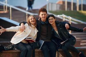 Embracing, each ,other. Three young students are outside the university outdoors photo