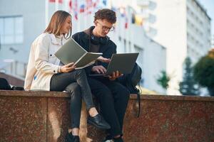 Front view.,, Two young students are sitting outdoors against university photo
