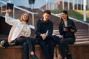 With, notepad. Three, young students are outside the university outdoors photo