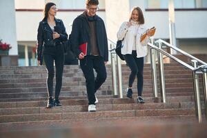 Walking ,down ,the stairs. Three young students are outside the university outdoors photo