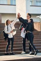 Giving high, five to each other. Three young students are outside the university outdoors photo