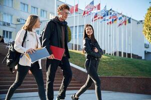 Going by the stairs. Three young,, students are outside the university outdoors photo