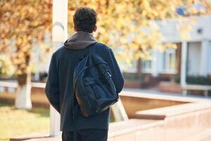 Back view. Young student is outside the university, in black clothes photo