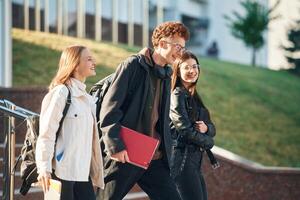 Holding, notepads in hands. Three young students are outside the university outdoors photo