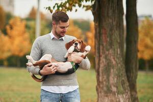 Young man is standing in the park and holding his cocker spaniel dog in hands photo