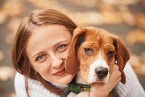 Sitting, holding, animal and looking into the camera. Young woman is with her dog in the park photo