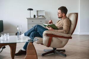Male psychologist is,, sitting in the chair with notepad in the office photo