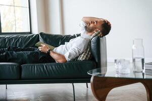 Tired man, in formal clothes is lying down on the black sofa photo
