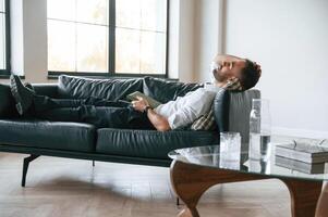 Tired,, man in formal clothes is lying down on the black sofa photo