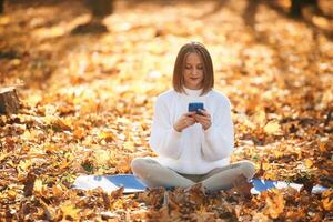 Woman is sitting in ,the, autumn park or forest with smartphone in hands photo