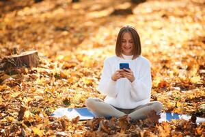 Woman, is sitting in th,e autumn park or forest with smartphone in hands photo