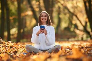 Woman ,,is sitting in the autumn park or forest with smartphone in hands photo
