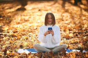 Woman is, sitting in the autumn park or forest with smartphone in hands photo