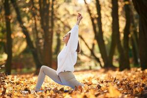 Trees at background, doing, exercises. Young beautiful woman is doing yoga in the autumn park photo