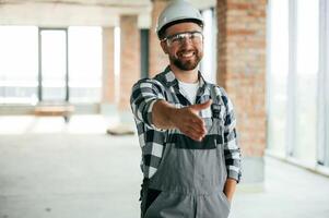 Giving the hand to shake, nice to meet you gesture. Construction worker in uniform in empty unfinished room photo