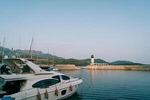 Moored motor yachts near the shore overlooking the white lighthouse on the breakwater photo
