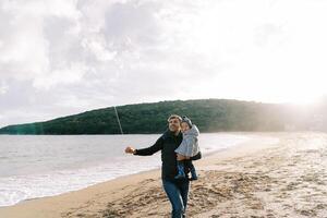 Dad with a little girl in his arms stands on the seashore with a kite rope in his hand photo