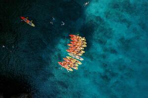 Captain boat sails towards a row of kayaks in the deep turquoise sea. Top view photo