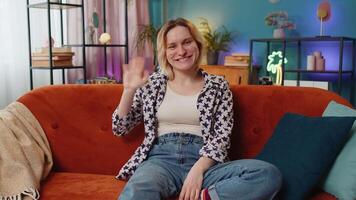 Portrait of young woman smiling at camera and waving gesturing hello hi greeting or goodbye at home video