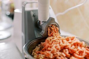 Electric meat grinder twists meat into a pan on the table photo