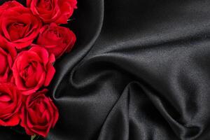 Fresh red roses are arranged artistically on luxurious black silk fabric, showcasing a blend of nature and elegance. photo