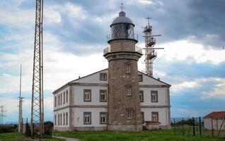 Historic lighthouse with a stone tower and white building under a cloudy sky photo