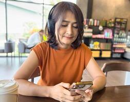 Woman sitting at the cafe holding smartphone and using headphones listen to music, watching social media networks while, typing chatting message, relaxing on vacation lifestyles concepts photo
