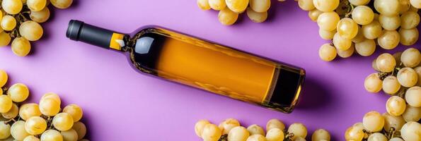 Bottle of white wine lying on purple background decorated with white grapes photo
