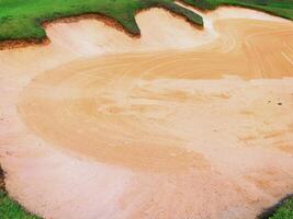 sand bunker on golf course with visible rake patterns under sunlight photo