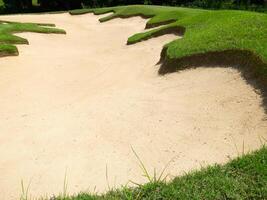 Empty golf bunker with smooth patterned sand surface and surrounding green grass photo