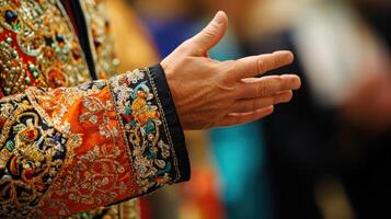 A closeup of a distinguished diplomats hand gesturing expressively while speaking with intricate embroidery on the sleeve of a traditional attire in the foreground emphasizing the cultura photo