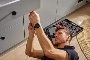 Carpenter installing and adjusting drawer front in modern kitchen cabinet photo