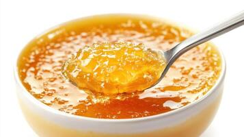 Orange marmalade in a white bowl. A spoon holds a portion of sweet citrus preserve with visible fruit pieces and sugary glaze. photo