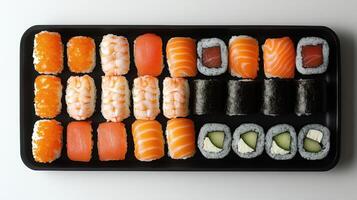 Assorted sushi pieces on black tray. Different types of sushi with salmon tuna shrimp and cucumber on white surface. Top view of sushi arrangement. photo