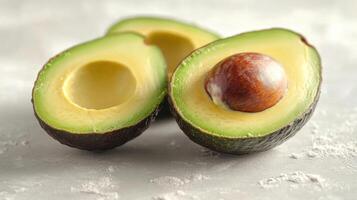 Three avocado halves on a gray surface with white powder. The avocado in front has a seed while the others are seedless. photo