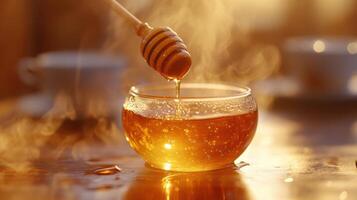 Close up of honey dripping from wooden dipper into small glass bowl with steam on warm surface with cups blurred in background photo