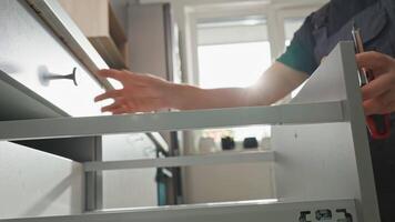 Man assembling kitchen drawer in cabinet using screwdriver. Handyman installing and adjusting drawer slide mechanism in contemporary kitchen. Furniture installation video