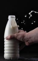 Hand holds milk in a bottle on a black background with a splash photo