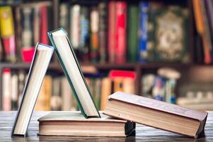 Three books on a table in front of a bookshelf photo